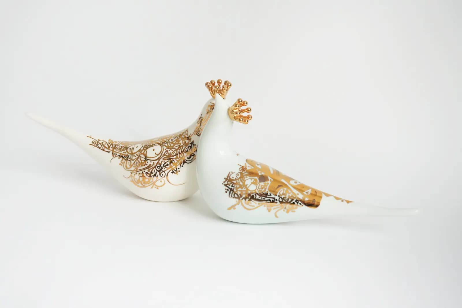 Two porcelain doves inscribed with gold Persian calligraphy, each wearing a gold crown