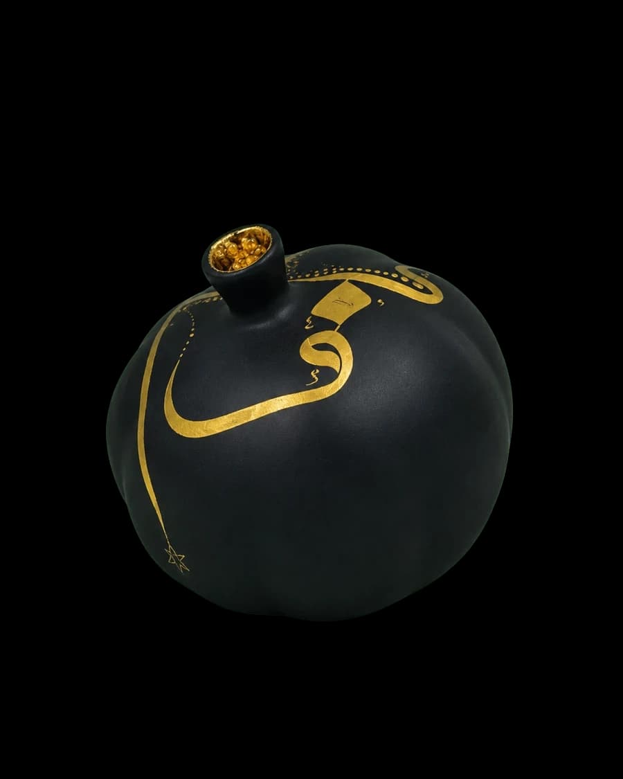 Matte black ceramic pomegranate with a crown of gilded seeds and a curling gold line